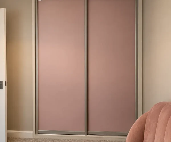 Dusty pink sliding wardrobes with two plain full-height doors and slim metallic frames in a softly decorated bedroom.